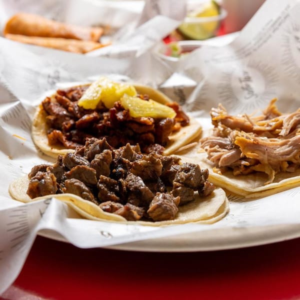 Three delicious tacos with various fillings, including pork and pineapple, on a white plate.