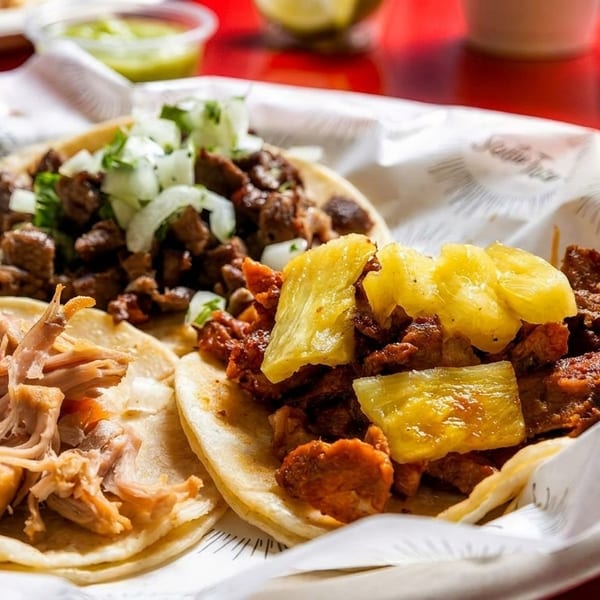 Three Santo Taco street tacos with various fillings, including pork, beef, and pineapple.