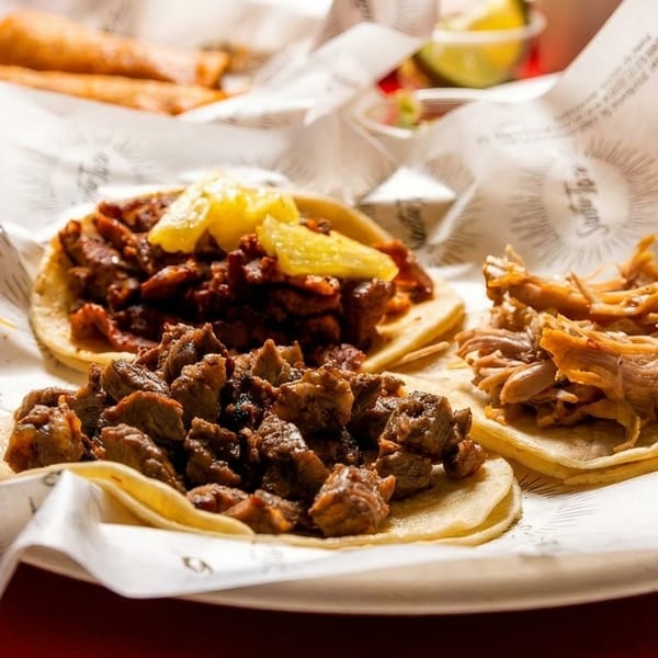 Three delicious tacos with various meat fillings and pineapple on branded paper.